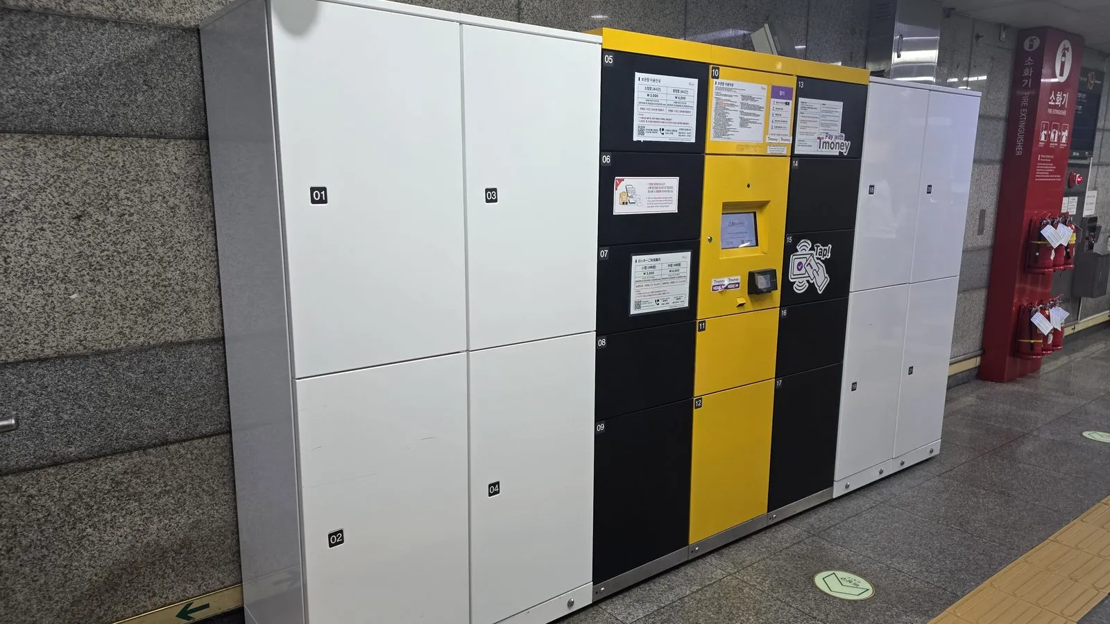 A bank of station coin lockers in three sizes, with a yellow payment screen set into the middle of them