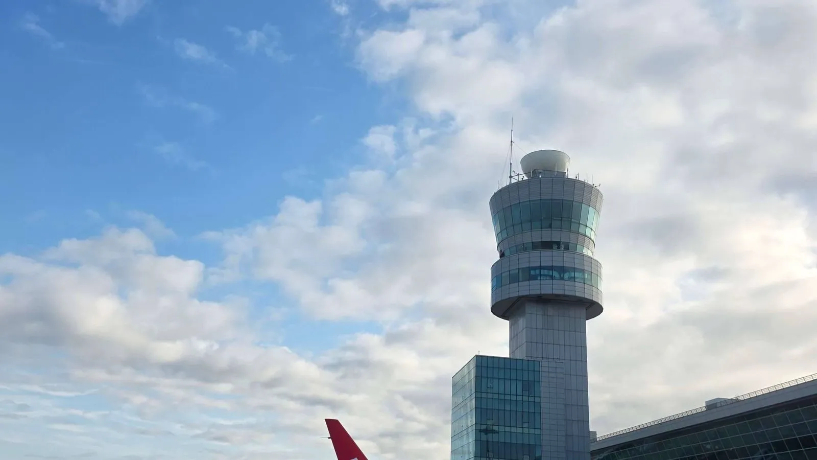 The control tower at Incheon International Airport under broken cloud, with the terminal roof to one side and the red tail fin of a parked aircraft below