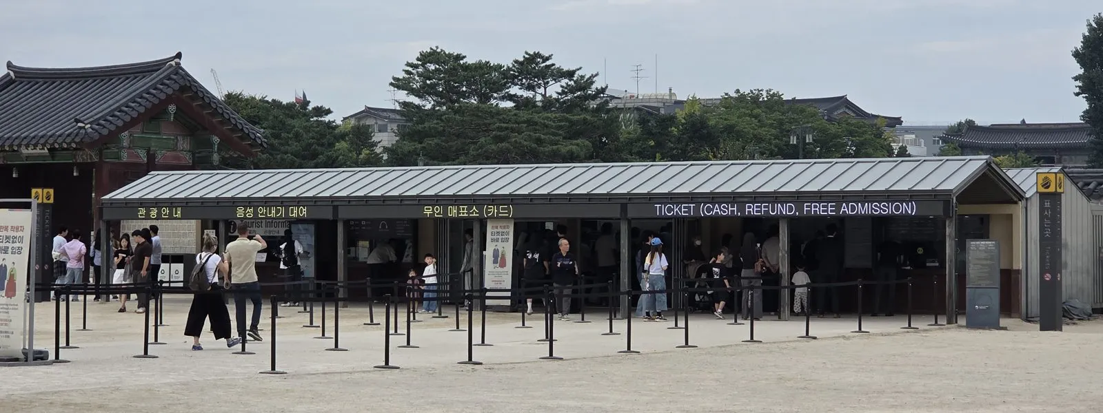 The ticket office building at Gyeongbokgung, with its windows labelled Tourist Information, Audio Guide Rental, Self-Service Ticketing and Ticket, the last one marked cash, refund and free admission
